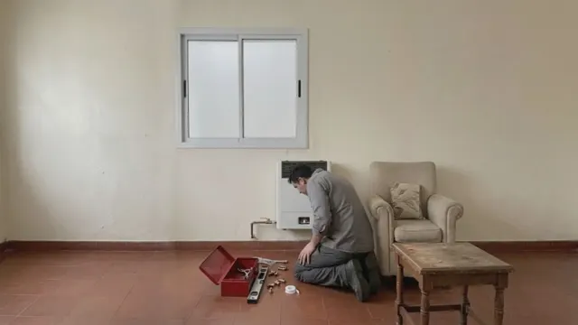 Gasista instalando una estufa de tiro balanceado en el living, con la llave de paso y los accesorios en el piso